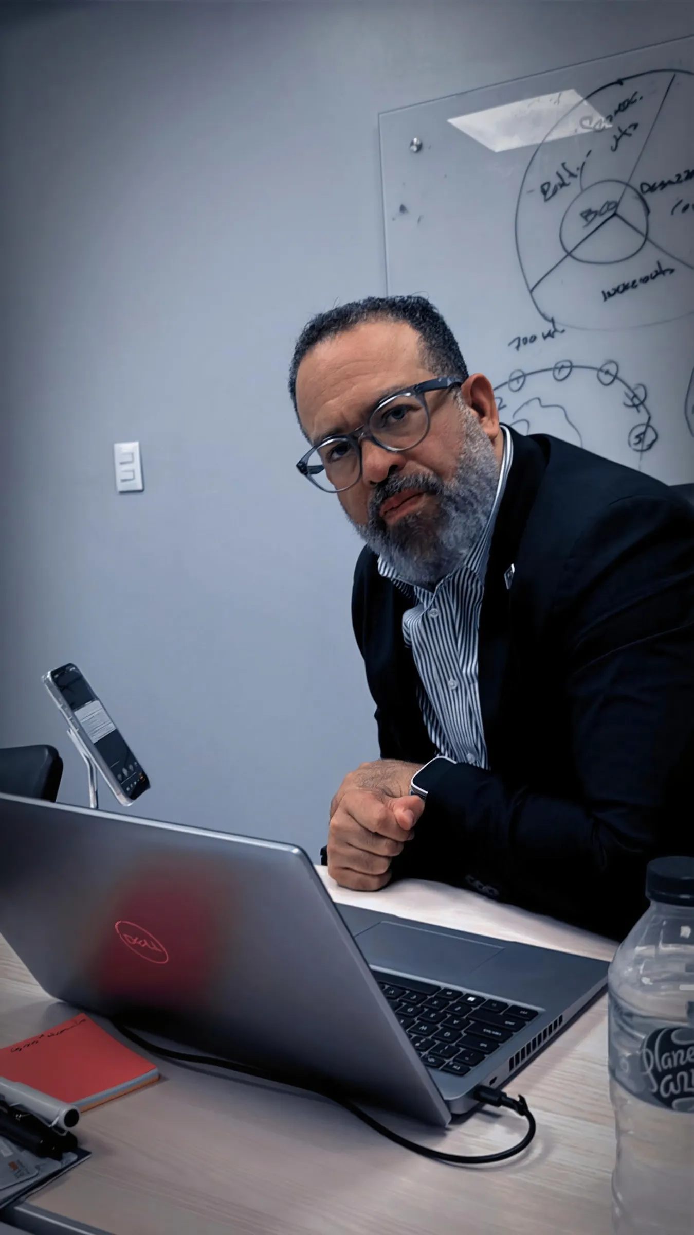 Henry L. Ogando, apoyado en la mesa de una sala de trabajo, mira a cámara con un portátil abierto delante